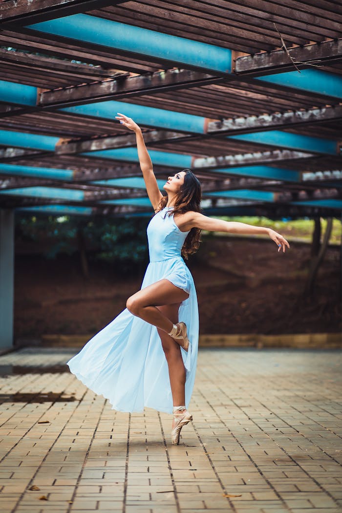 Graceful ballerina dances outdoors in a flowing blue dress.